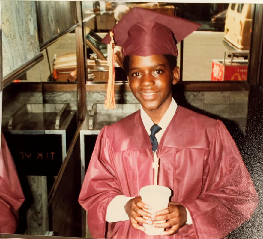 David Smiling graduate wearing cap and gown inside McDonald&rsquo;s in Harlem at 132nd Street and Lenox Avenue.